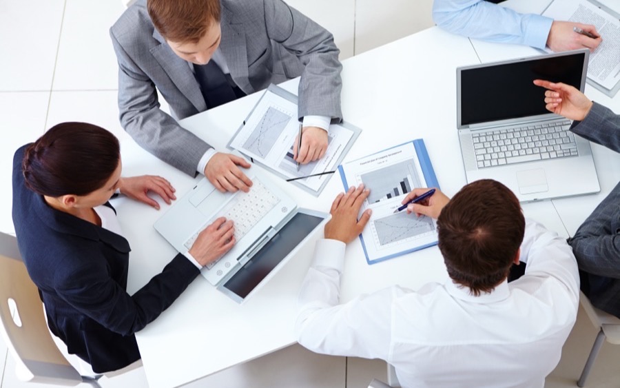 Colleagues working across laptops and printed data at a shared table
